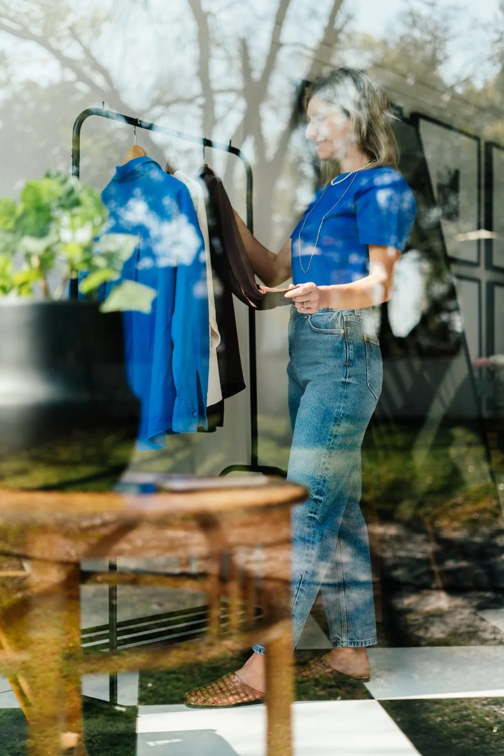 Jeanine choosing a blue shirt from her clothes rail, seen through the window