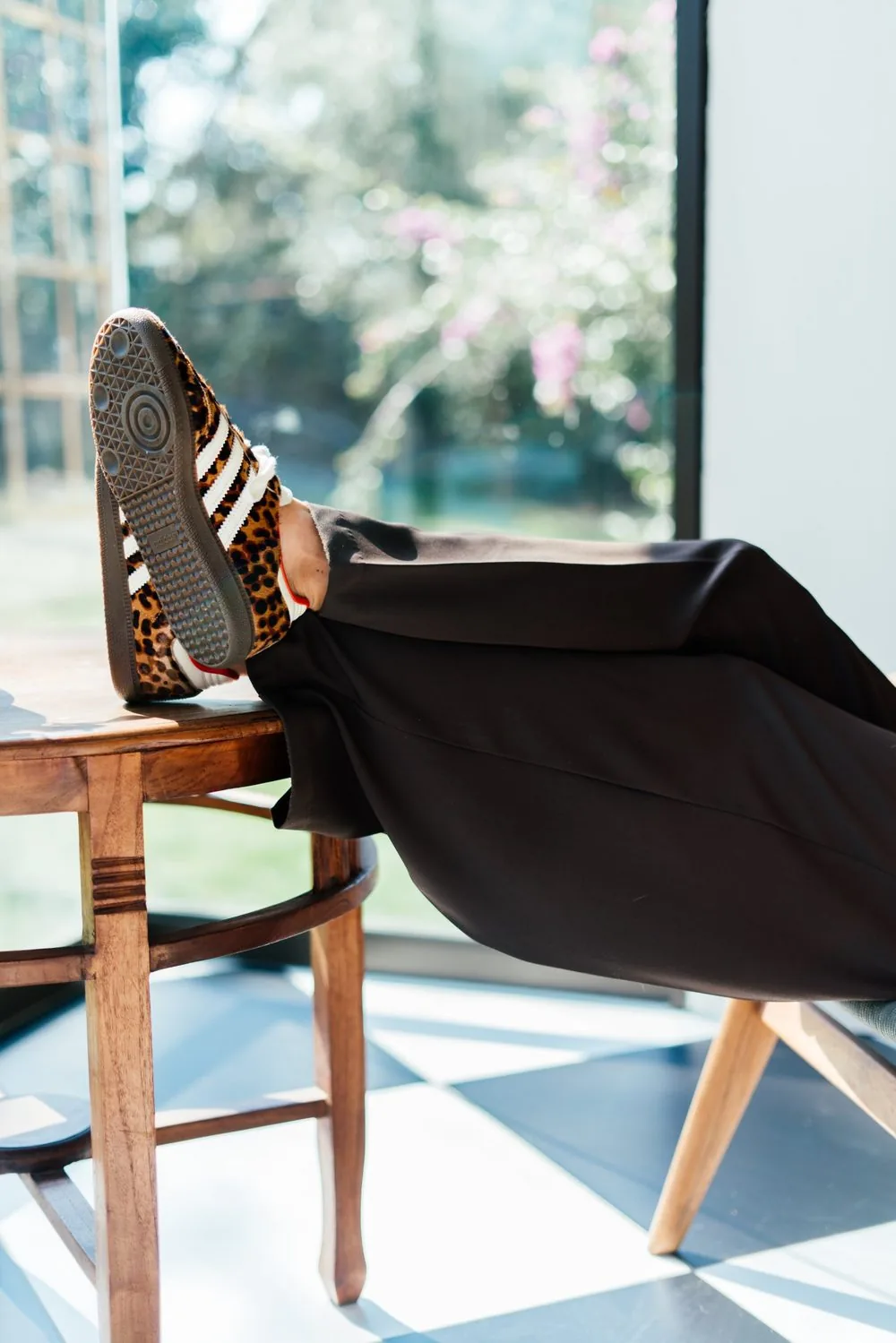 Leopard-print sneakers, feet up on a wooden chair by the window