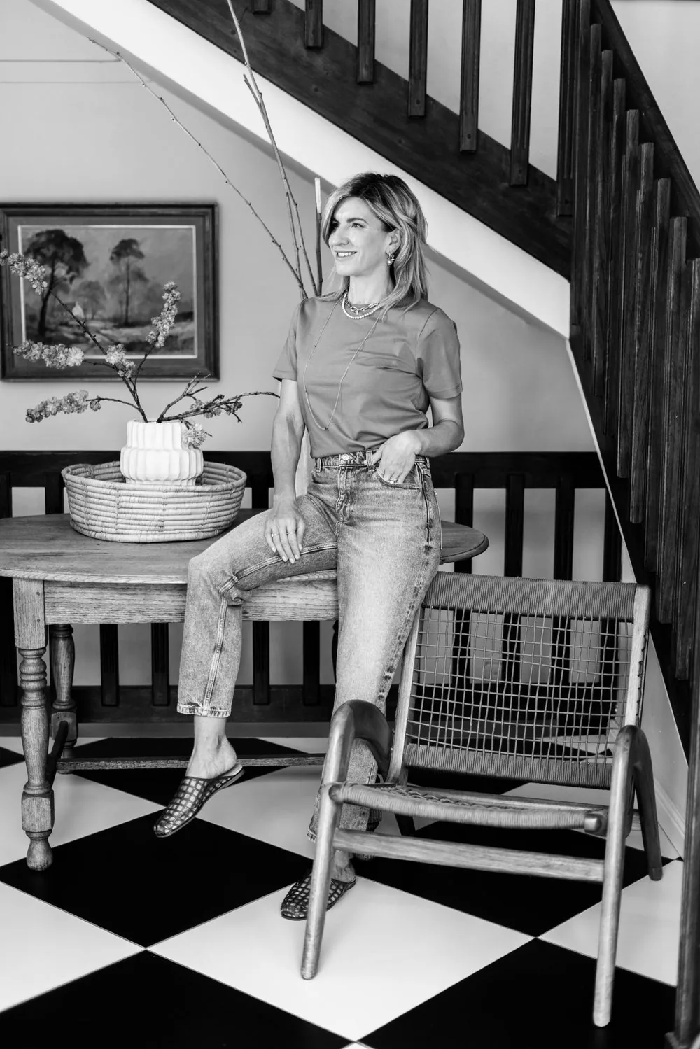 Jeanine seated on a chair by the stairs, in black and white